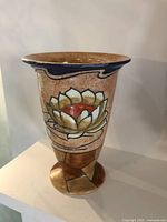 Front view of vintage Burleigh Ware vase with water lily decoration on mottled beige background, flared rim with blue detailing, and geometric pedestal base.