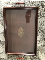 Full view of rectangular dark wood tray with glass top and central geometric motif, with wooden handles visible.