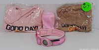 View of two folded 'Good Day!' sweatshirts in pink and brown colors with a pink adjustable dog collar featuring an AirTag holder.