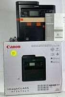 Canon MF267dw II printer on top of its original cardboard box with setup guide visible beside it.