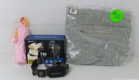 Lot overview showing T30 dog training collar in box with remote, pink chew toy, and folded grey apparel with zipper pocket.