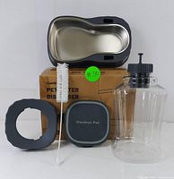 Gardner Pet water dispenser components: stainless steel bowl attached to plastic base, clear water reservoir with screw cap, square lid, cleaning brush, ring support, and box.