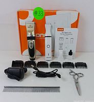 Full kit with pet clippers, paw trimmer, six guide combs, scissors, charger, cable, maintenance oil, metal comb, and manual in front of orange and white box