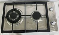Top view of stainless steel 2-burner gas cooktop with black cast iron grates and control knobs