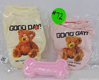 Two XS pet apparel pieces in cream and pink with teddy bear graphics and "Good Day!" text, plus a pink bone chew toy in front.