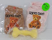 Brown and pink pet shirts side by side in sealed plastic packaging with a yellow bone chew toy in front