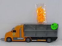 Side view of yellow toy transport truck alongside a sealed bag of orange accessory pieces