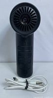 Front view of black CAGIWIRU electric air duster device showing circular nozzle and white USB charging cable below it