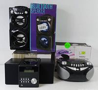 Proscan Bluetooth speaker next to its box, Proscan radio cassette player next to its box, and Proscan CD micro system with its two speakers and box in the background.