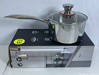 Side view of the saucepan placed on its box showing handle and lid.