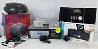 Full lot showing all three audio devices and original boxes: Bluetooth CD micro system with speakers (silver and black), portable black CD boombox on red box, and kitchen Bluetooth radio in box.