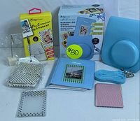 Full assortment of instant camera accessory kit items arranged on a surface including blue leather case, photo albums, boxes of clip and frame kits, clear frames, and camera strap.