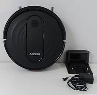 Top view of the black Airzeen robot vacuum next to its charging dock and power adapter cable.