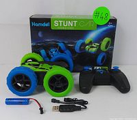 Double-sided green and blue Hamdol stunt car, black and blue 2.4G remote, rechargeable battery, USB charging cable, and original box side view