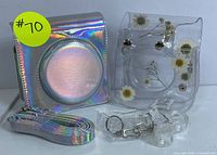 Lot with holographic camera bag, matching strap, clear floral instant camera case, clips, and keychains arranged on table