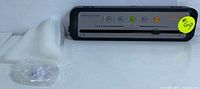 Megawise vacuum sealer unit with control panel, indicator lights, and buttons, next to a roll of vacuum bags and sealing accessories.
