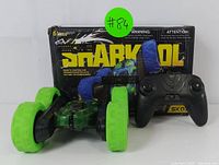 Photo showing remote control stunt car with black body and bright green wheels along with black ergonomic controller, and original packaging box with Snarkool branding.