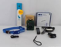 Full set with blue LED dog collar in packaging, green ultrasonic bark control device, Razia remote dog trainer with strap, charging cables, and lanyard.