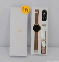 Original white box with gold Erkvei logo containing gold-tone smart watch with mesh band, extra white and beige straps, and charging cable.
