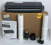 FoodSaver FM2000 vacuum sealer with two rolls of sealing bags and owner's manual on cardboard box.