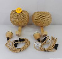 Photo showing two spherical woven rattan wall sconces mounted on light wooden bases, with attached braided electrical cords coiled in front.