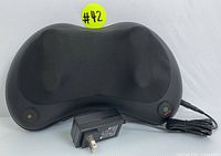Front view of the black heated massage pillow showing two massage nodes, power and heat buttons, and power adapter connected.