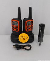 Two Midland walkie-talkies placed on a black dual charging dock. USB charging cable and compact flashlight shown alongside.