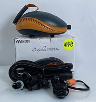 Electric air pump in gray and orange on top of original box, coiled hose, multiple black nozzle adapters, and black power cable with 12V car adapter