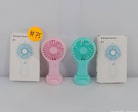 Two handheld rechargeable fans, one pink and one blue, shown upright side by side with their original white boxes labeled Eternal classics F1 behind them.