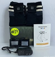 Photo of the pair of black heated socks with gray and white stripes on cuff, two battery packs, charging adapter, and instruction pamphlet on white background