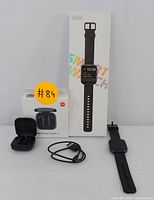 Black smart watch with rectangular display, charging cable, box showing 'Smart Watch' text; black wireless earbuds with charging case and box with Xiaomi branding.