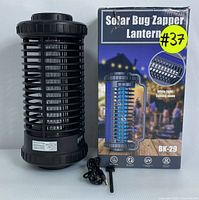 Front view of black plastic cylindrical solar bug zapper lantern BK-29 with box showing product branding, features, and model number