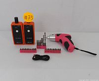 Photo showing pair of walkie-talkies, pink cordless screwdriver, bit sets, and charging cable arranged on a white surface with a #73 tag.