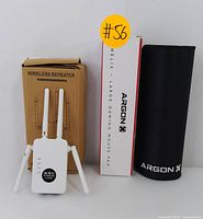 White WiFi repeater with four external antennas in front of brown box labeled Wireless Repeater, LED indicators and WiFi Amplifier 1200M label visible.