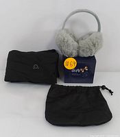 Soft grey faux fur ear warmers on a padded headband alongside a folded black heated scarf and a small black drawstring pouch