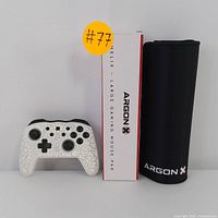 The gaming controller displayed on the left, ArgonX large gaming mouse pad in packaging on the right beside its box, sitting on a flat surface.