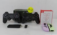 Two black 2.4G wireless gaming controllers with ergonomic grips, original box, USB dongle, and USB charging cable, plus pink and green Nintendo Switch J-Con pads with their packaging on white background.