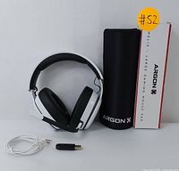 Photo showing white and black wireless gaming headset, USB adapter, 3.5mm cable, and Argon X mouse pad rolled in carrying case.