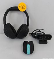 Photo showing the black wireless over-ear headphones, black HD webcam with built-in microphone, and black rechargeable wireless mouse with turquoise accent arranged side by side.