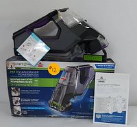 BISSELL Pet Stain Eraser PowerBrush device on top of its original packaging alongside the user manual.