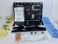 TV mount wall bracket components laid out on a surface including mounting plates, arms, screws in labeled bags, and installation manual