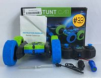 Photo showing all lot contents, including the RC stunt car, remote control, charger cable, screwdriver, blue accessory part, instruction manual, and box.