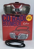 Front view of red Proscan CD radio boombox placed on top of its original box showing front speaker grilles, digital display, and control buttons.