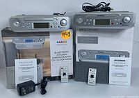 Photo of both Proscan and Sylvania Bluetooth under-cabinet CD clock radios on top of their boxes, with remote controls, power adapters and manuals laid out.