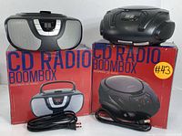 Two Proscan portable CD boomboxes sitting on their original boxes, showing power cords and external appearance