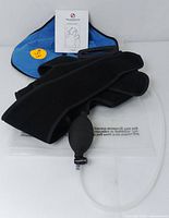 Image showing black shoulder support wrap with inflation hand pump and instruction manual on white background.