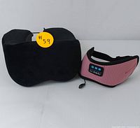 Black memory foam travel neck pillow with drawstrings and pink Bluetooth sleep mask with control buttons side by side on white background.