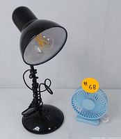 Photo of black desk lamp and blue USB fan showing both items powered off with cords coiled.