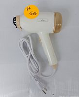 Side view of the handheld steamer showing white and beige body, power button, and attached white power cord with two-prong plug.
