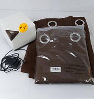 Photo of the white electric humidifier with geometric design, power adapter, and folded brown curtains with silver grommets.